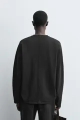 Camiseta de manga larga con corte relajado, confeccionada en tejido compacto de algodón. Presenta cuello redondo acabado en rib y detalle de costura central en la espalda.