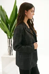 Blazer de mujer color gris oscuro con textura de jean/lino, corte oversize, hombreras, bolsillos frontales y pespuntes a contratono. Cierre frontal con botones.