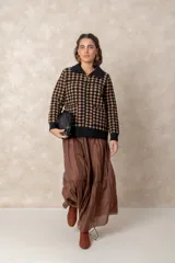 Chaqueta de punto grueso con patrón geométrico de cuadros en blanco y negro. Presenta cuello camisero, cierre frontal con cremallera y tirador circular, bolsillos frontales y puños acanalados.