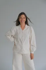 Blusa de color beige con cuello mao y cierre frontal de botones. Presenta mangas largas abullonadas con puños ajustados y un diseño con bordados en relieve de patrones orgánicos en toda la prenda.