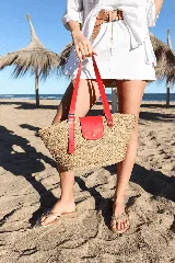 Bolso tipo canasto de paja con detalles en cuero rojo, incluyendo un bolsillo externo con solapa y cierre con botón a presión, y correa regulable.