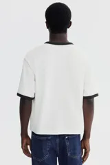 Remera de algodón en color blanco con cuello y bordes de mangas en contraste color negro. Presenta un diseño de corte holgado con hombros caídos y bajo recto.