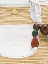 Bolso tipo canasta de tamaño pequeño, confeccionado en paja trenzada con detalles en cuero verde. Cuenta con asas cortas, solapa frontal con logo grabado y un colgante decorativo con cuentas de madera.