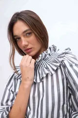 Blusa de algodón con estampado de rayas grises y blancas, cuello alto fruncido con volados y mangas largas con puños elásticos.