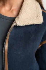 Campera tipo gamulán de corte oversize, color azul marino con interior y cuello de corderito en tono beige. Presenta detalles de costuras y bordes en cuero sintético color marrón, cierre frontal y mangas largas.