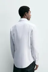 Camisa de corte regular fit confeccionada en tejido de algodón con textura. Presenta cuello italiano, manga larga con puños abotonados y cierre frontal de botones.