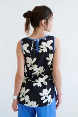 Top sin mangas de color blanco con escote en V y diseño holgado. Presenta un estampado artístico frontal en tonos azul y rojo, con terminaciones de vivo a contratono en color marrón.