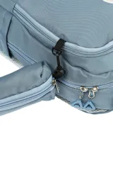 Mochila escolar de tela color azul claro, con múltiples compartimentos con cierre, bolsillo frontal con cierre y un pequeño accesorio colgante cilíndrico a juego. Presenta un parche circular con un emoji sonriente en el frente.