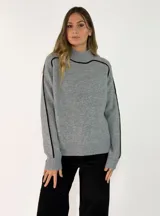 Sweater de punto gris con cuello alto y detalles de líneas negras contrastantes en los hombros y mangas. Presenta puños y ruedo acanalados.