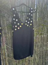 Vestido negro sin mangas con escote en V profundo, adornado con tachas metálicas redondas plateadas en la zona del busto y los hombros.