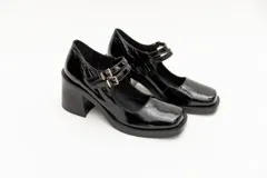 Guillerminas de cuero charol negro con punta cuadrada, taco ancho y correa sobre el empeine con doble hebilla dorada.