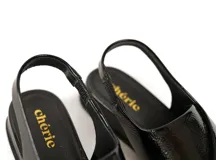 Sandalia de charol negro con tiras cruzadas en el empeine y tira elástica en el talón. Cuenta con plantilla de cuero acolchada y plataforma ligera con un tacón de 3cm.