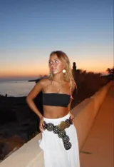 Cinturón ancho de cuero negro con diseño de círculos superpuestos. Presenta apliques metálicos circulares en tono dorado envejecido, algunos lisos y otros con grabado tribal/étnico. Los círculos de cuero tienen ojales metálicos pequeños alrededor de los apliques grandes.