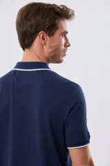 Remera polo de piqué azul marino, con cuello y puños de mangas cortas con ribete blanco en contraste, cierre frontal de dos botones y pequeño logo bordado en el pecho.