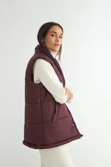 Chaleco acolchado color chocolate con interior y cuello de corderito sintético. Presenta cierre frontal con botones a presión y bolsillos laterales.