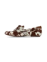 Mocasín náutico confeccionado en cuero con pelo con estampado animal print de vaca en tonos marrón y blanco, con cordones de cuero marrón en el empeine y ojales metálicos.