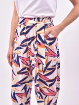 Pantalón babucha de tiro alto con cintura fruncida y lazo para ajustar. Estampado de hojas tropicales en tonos naranja y marrón sobre fondo blanco.