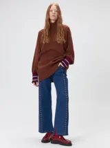 Pullover de punto color rojo, con cuello tortuga, corte holgado y mangas largas con puños acanalados en contraste con rayas blancas. Presenta un logo bordado en el pecho.