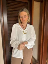 Camisa blanca de tela liviana con textura sutil, presenta detalles calados verticales en el delantero y volados delicados en los hombros. Posee mangas largas con puños y cierre frontal mediante botones.