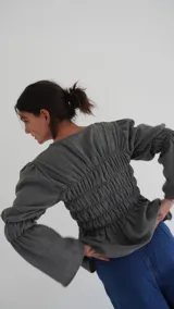 Camisa a cuadros azul y gris con cuello redondo y mangas largas abullonadas. Presenta detalle de fruncido en el frente y puños elásticos.