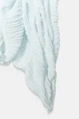 Top de cuello redondo color celeste con textura fruncida, mangas tipo capa y bajo asimétrico.