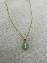 Collar con cadena dorada y dije de piedra natural pulida con cruz dorada incrustada. Disponible en tres colores: rosa, lila y blanco.