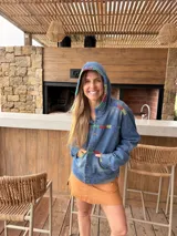Campera de jean azul con capucha y detalles de bordado artesanal multicolor en la capucha, el pecho, los bolsillos y las mangas. Cuenta con cierre frontal de botones, bolsillos delanteros y diseño cómodo.