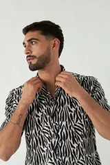 Camisa de manga corta con cuello cubano, confeccionada en viscosa con estampado de hojas en tonos azules. Presenta cierre frontal abotonado y corte slim.