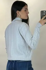 Buzo de hilo de punto con diseño de trenzas verticales, cuello alto y cadena metálica decorativa incorporada en la parte frontal.