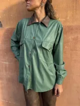 Camisa verde de cuero sintético con cuello marrón, cierre frontal con botones, dos bolsillos con solapa en el pecho y cinturón marrón.
