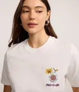 Remera blanca de manga corta y cuello redondo con un gran estampado trasero inspirado en el Tamagotchi, con texto en japonés y elementos gráficos de estilo retro.