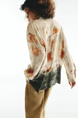 Camisa de manga larga con cuello solapa y cierre frontal con botones, con diseño tie-dye en tonos beige, naranja y verde oscuro en el sector inferior.