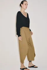 Pantalón de tiro medio confeccionado en mezcla de lyocell, con diseño de pliegues delanteros superpuestos y bolsillos laterales ocultos en costura.
