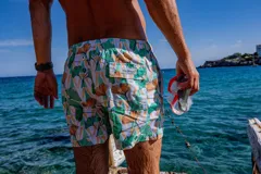 Short de baño Von Braun con estampado botánico de hojas en tonos verdes y naranjas sobre fondo blanco. Cuenta con cintura elástica, dos bolsillos laterales y un bolsillo trasero con solapa y etiqueta de la marca. Incluye interior con mesh hipoalergénico y tela de secado rápido.