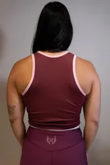 Musculosa deportiva ajustada color vino tinto, con cuello redondo y ribetes en color rosa claro. Presenta un estampado central con un sol estilizado y la palabra "Hermod" en cursiva.