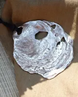 Collar artesanal con dije central de metal con textura orgánica irregular que evoca una ostra. El dije está montado sobre un cordón de algodón natural, permitiendo un uso versátil y regulable.