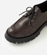 Mocasín tipo dockside color marrón oscuro con acabado texturizado, ajuste frontal con cordones y suela track robusta de goma.