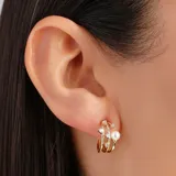 Aros dorados con forma de argolla triple, con incrustaciones de strass y una perla.