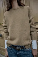 Jersey de punto de cuello redondo y manga larga, con diseño de corte recto y acabados en rib. Presenta detalles de calados decorativos en los laterales.
