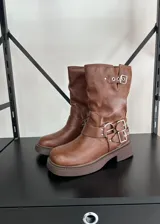 Bota tipo biker de caña media en cuero vegano color marrón, con suela track y múltiples correas con hebillas metálicas plateadas en el tobillo y la parte superior de la caña.