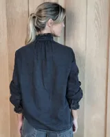 Camisa de denim con volados verticales a lo largo de la botonadura frontal y cuello alto. Presenta mangas largas con puños elásticos y detalle de volados en los mismos.