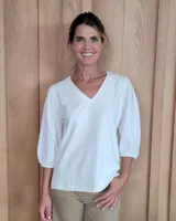 Remera blanca de cuello en V, con mangas tres cuartos abullonadas y puños elásticos.