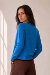 Cardigan de punto azul con ribetes en contraste negro, cuello redondo, cierre frontal con botones y bordado pequeño en el pecho.