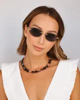 Lentes de sol con armazón ovalado sin aire, lentes oscuros y detalles metálicos dorados.
