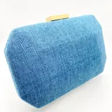 Clutch rígido rectangular forrado en lino azul, con cierre dorado en la parte superior y asa de cadena metálica dorada.