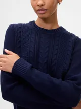 Buzo de algodón color crema con cuello redondo y diseño de punto trenzado en el frente.