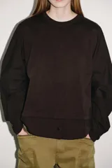 Camiseta oversize de cuello redondo y manga larga con puños abotonados. Confeccionada en algodón, presenta un diseño con combinación de tejidos a tono y bajo asimétrico.