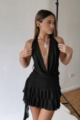 Vestido corto negro con escote halter y drapeado en el busto. La falda es corta con volados y un detalle de lazo lateral.