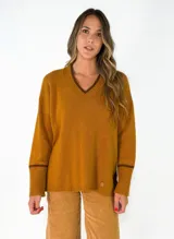 Sweater de punto azul marino con cuello en V, mangas largas con puños acanalados y detalle de línea en color marrón en el cuello y puños. Presenta un pequeño aplique decorativo en la parte inferior.