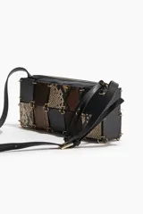Cartera bandolera rectangular con correa ajustable negra. El cuerpo del bolso está confeccionado con un patrón de patchwork de cuadrados en cuero negro liso, gamuza marrón y estampado de piel de serpiente en tonos beige y marrón. Los paneles están unidos por grapas metálicas doradas. Posee cierre superior y forro interior.